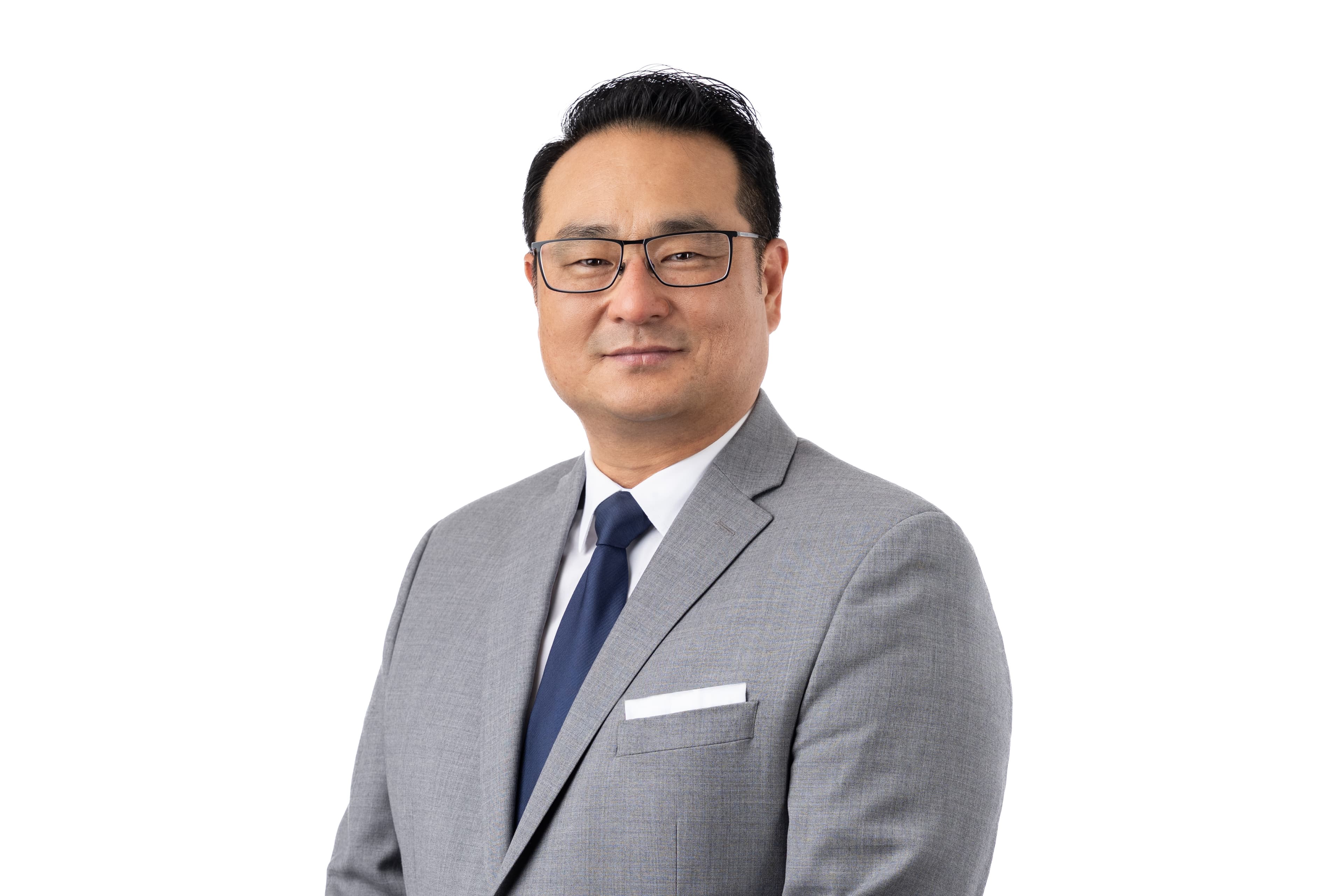Middle-aged Asian man in a grey suit, blue tie, and glasses on white background.